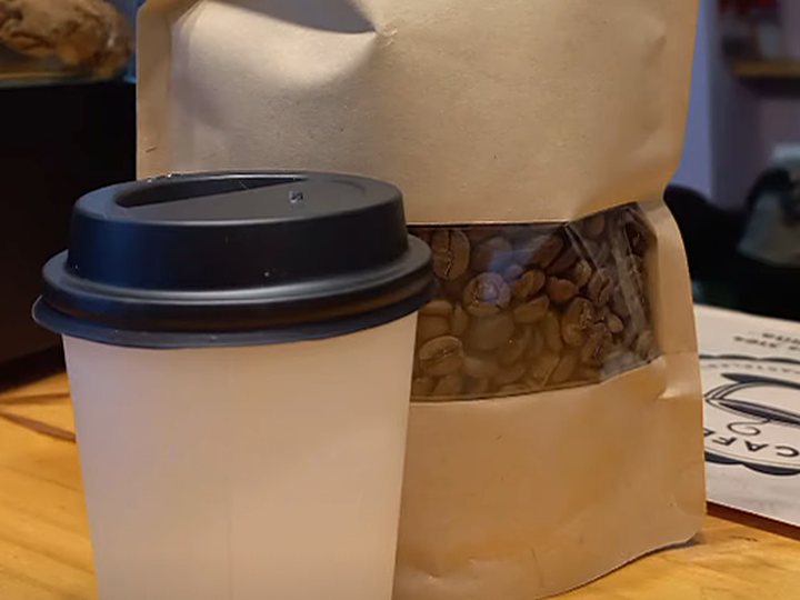 Un vaso de café para llevar junto a una bolsa de café en granos